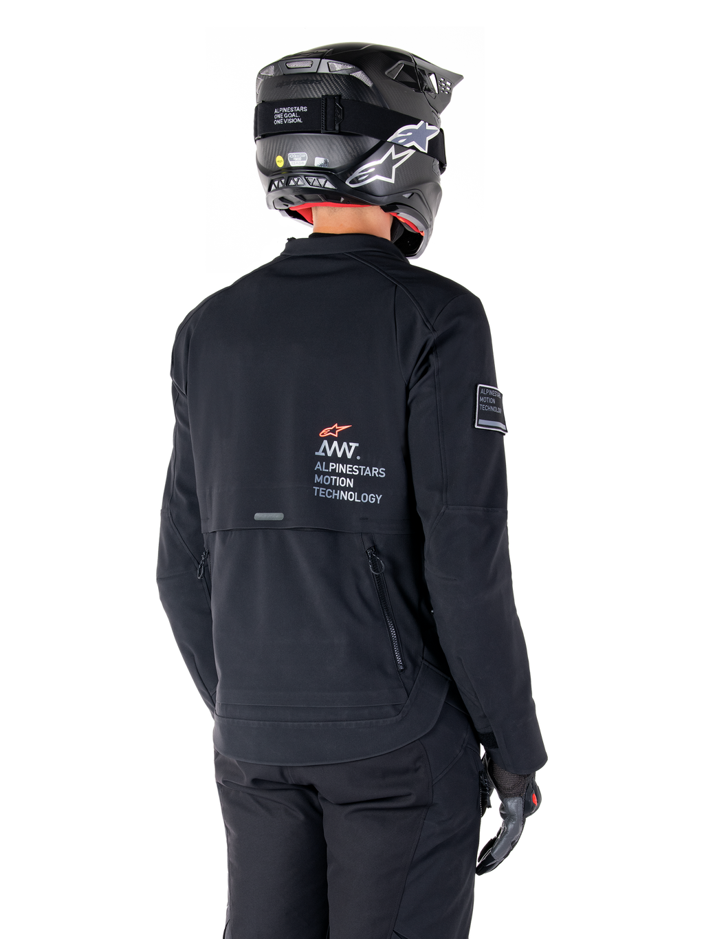 Vy bakifrån på en förare som bär Alpinestars AMT-8 Stretch Drystar® XF-jacka i svart, med 'AMT Alpinestars Motion Technology'-logotyp på ryggen, teknisk ventilation med dragkedja, kombinerad med en svart motorcykelhjälm och handskar