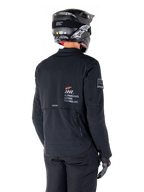 Vy bakifrån på en förare som bär Alpinestars AMT-8 Stretch Drystar® XF-jacka i svart, med 'AMT Alpinestars Motion Technology'-logotyp på ryggen, teknisk ventilation med dragkedja, kombinerad med en svart motorcykelhjälm och handskar