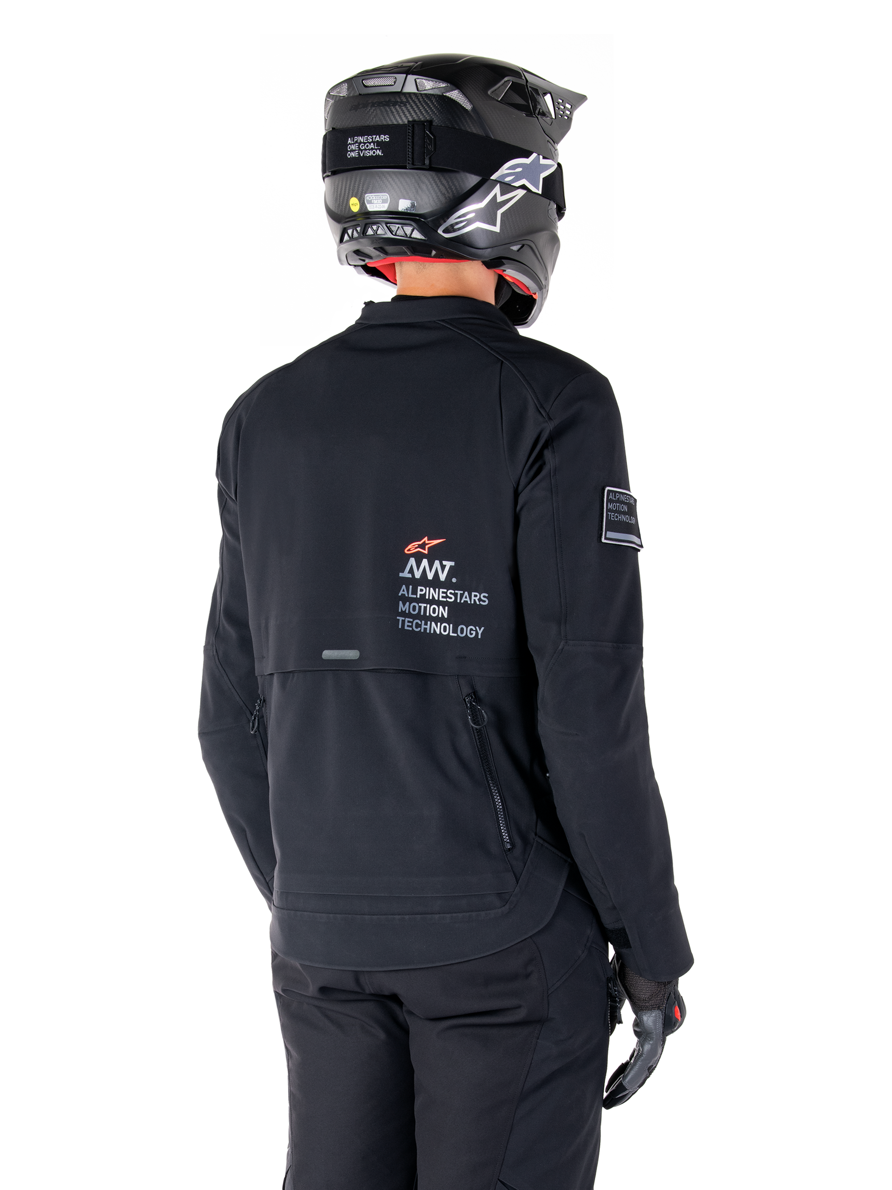 Vy bakifrån på en förare som bär Alpinestars AMT-8 Stretch Drystar® XF-jacka i svart, med 'AMT Alpinestars Motion Technology'-logotyp på ryggen, teknisk ventilation med dragkedja, kombinerad med en svart motorcykelhjälm och handskar