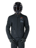 Alpinestars AMT-8 Stretch Drystar® XF-jacka, svart motorcykeljacka med orange Alpinestars-logotyp och grå AMT-branding, hög krage med dragkedja fram och ventilationsöppningar, bärs med svart hjälm och handskar, skyddande utrustning för adventure touring