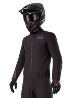 Förare som bär Alpinestars AMT-8 Stretch Drystar® XF Liner, svart vind- och vattentät stretchjacka med AMT-logotyp på bröstet och Drystar XF-märkning på ärmen, kombinerat med en svart adventurehjälm och skyddshandskar.