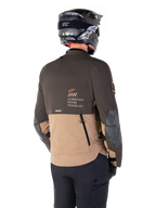 Alpinestars AMT-8 Stretch Drystar® XF-jacka, äventyrsmotorcykeljacka, mörkbrun och mörk khaki, vy bakifrån som visar AMT Alpinestars Motion Technology-logotyp, tvåfärgad textildesign med ventilationsdragkedjor bak och ryggutblås i skifferdesign, bärs med svart hjälm och körbyxor