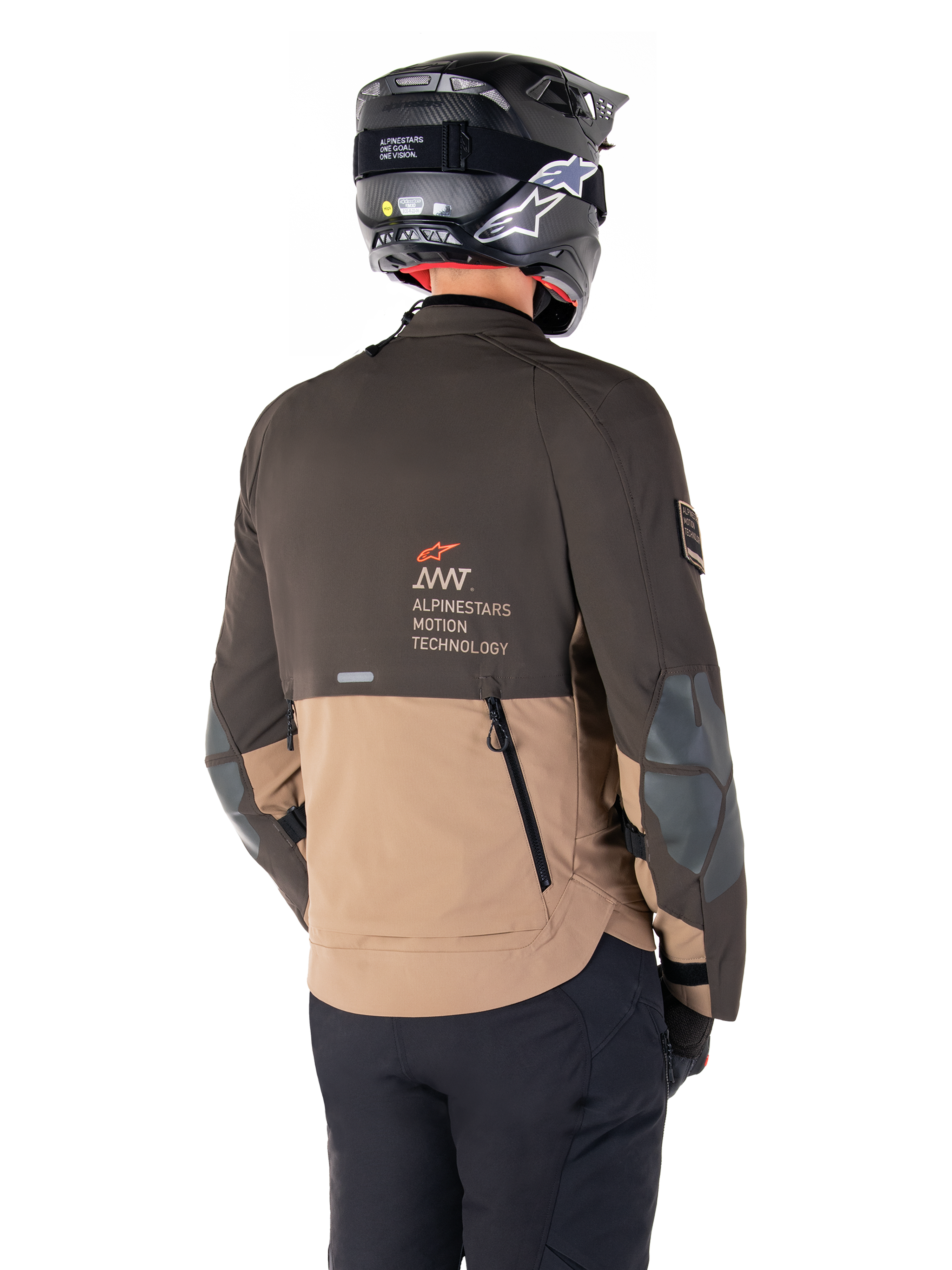 Alpinestars AMT-8 Stretch Drystar® XF-jacka, äventyrsmotorcykeljacka, mörkbrun och mörk khaki, vy bakifrån som visar AMT Alpinestars Motion Technology-logotyp, tvåfärgad textildesign med ventilationsdragkedjor bak och ryggutblås i skifferdesign, bärs med svart hjälm och körbyxor
