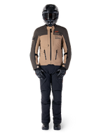 Alpinestars AMT-8 Stretch Drystar® XF-jacka, äventyrsmotorcykeljacka, mörkbrun och mörk khaki, bärs med svart hjälm, goggles, svarta handskar, svarta byxor och svarta stövlar, med ventilationsöppningar på bröstet och AMT-branding, matchande utrustning för äventyrstouring