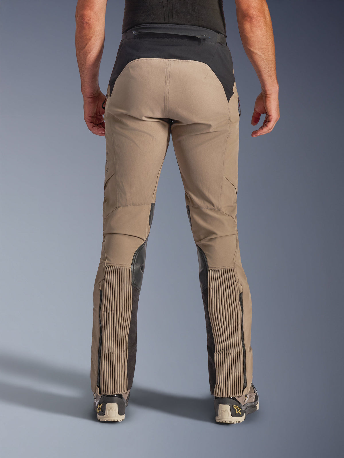 Alpinestars AMT-8 Stretch Drystar® XF Byxor, Walnut Black, vy bakifrån på modell, ljusbrun stretchtextil med svart ok i midjan och vadpaneler, med stora dragspelstretch-sektioner på underbenen, benöppningar med dragkedja och adventure-touring-passform