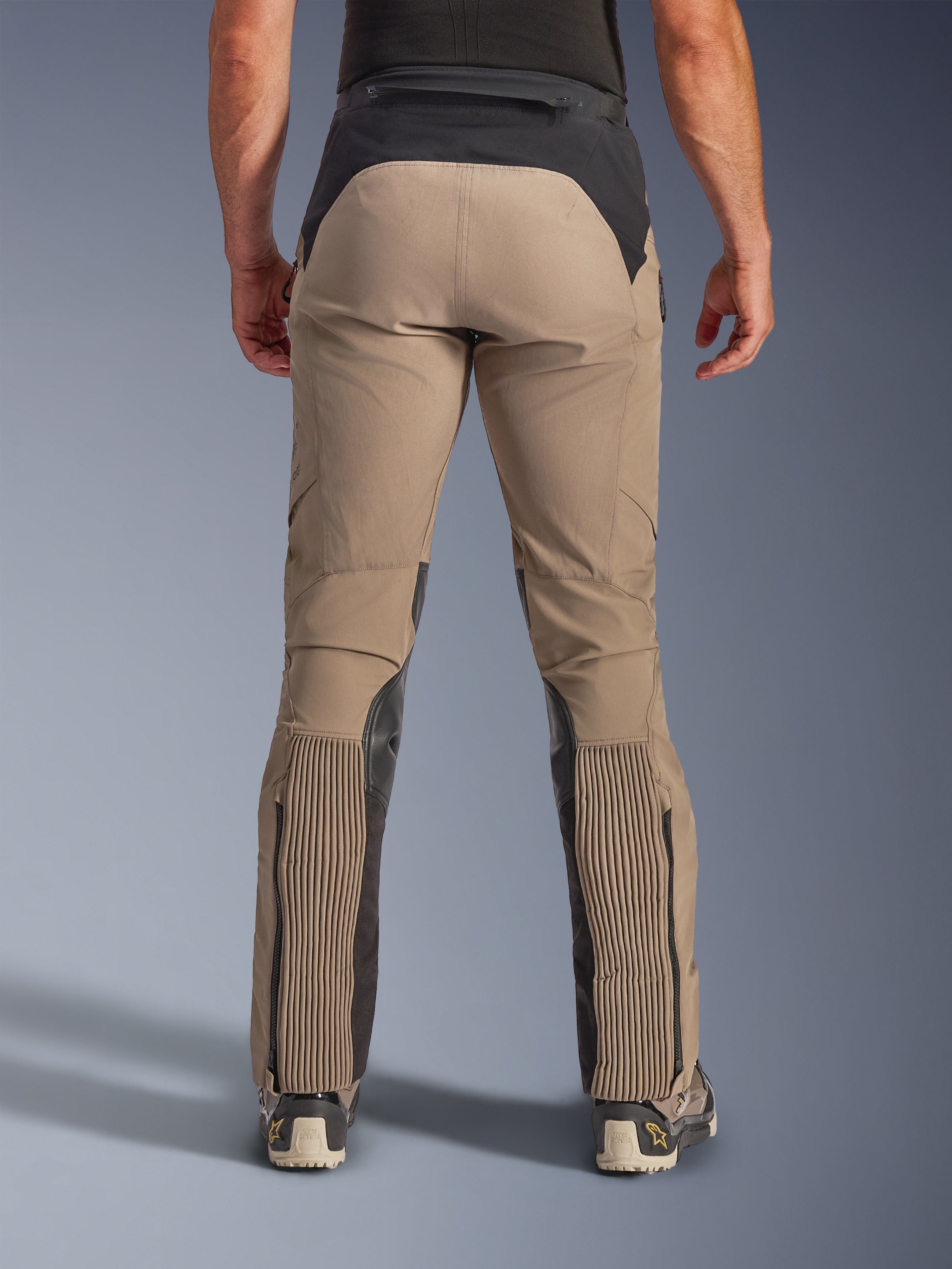 Alpinestars AMT-8 Stretch Drystar® XF Byxor, Walnut Black, vy bakifrån på modell, ljusbrun stretchtextil med svart ok i midjan och vadpaneler, med stora dragspelstretch-sektioner på underbenen, benöppningar med dragkedja och adventure-touring-passform