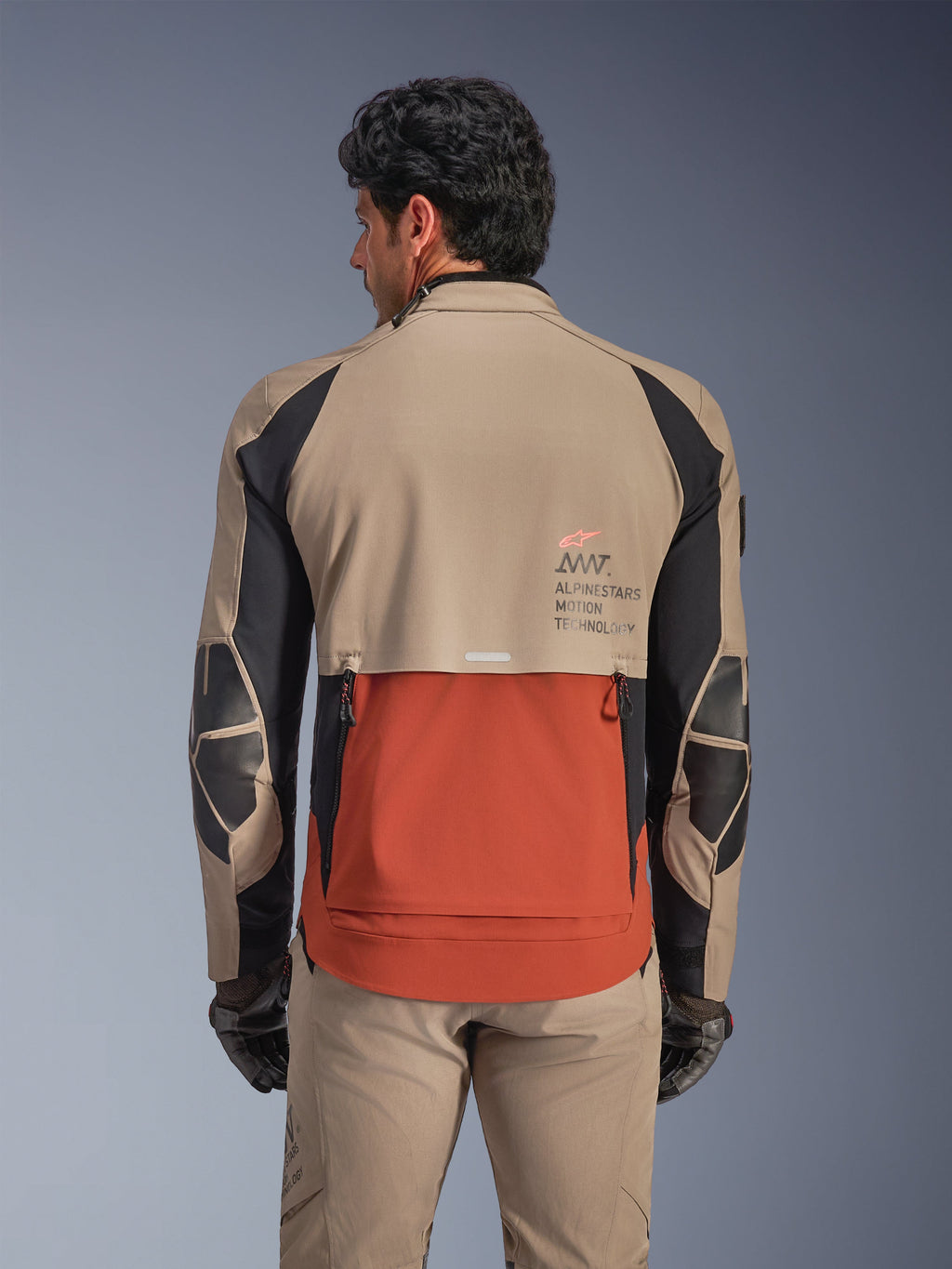 Alpinestars AMT-8 Stretch Drystar® XF Jacka, Walnut Rust Black, sedd bakifrån på modell, framhäver ryggutblåset med skifferdesign i rostfärg, valnötsbruna övre sektioner, svarta detaljer på ärmarna och Alpinestars Motion Technology-logotyp