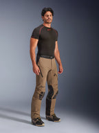 Alpinestars AMT-8 Stretch Drystar® XF-byxor i Walnut Black, adventure touring-motorcykelbyxor som bärs av en modell med en svart underställströja, med stretchmaterial, dragkedjeförsedda ventilationsöppningar på låren och skyddande knäpaneler.