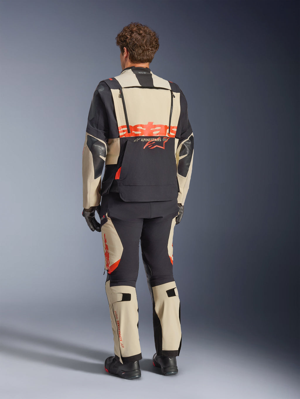 Alpinestars Halo Pro Drystar® XF laminerad jacka, Mastic Black, vy bakifrån, äventyrsmotorcykeljacka med stor orange 'astars'-logotyp över ryggen, bärs med matchande tekniska byxor och stövlar, modulär design för mångsidig terräng