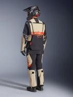 Alpinestars Halo Pro Drystar® XF laminerad jacka, Mastic Black, vy bakifrån av en förare iklädd ett komplett äventyrsställ med matchande byxor, svart äventyrshjälm och stövlar, med en framträdande röd Alpinestars-logotyp över ryggen.