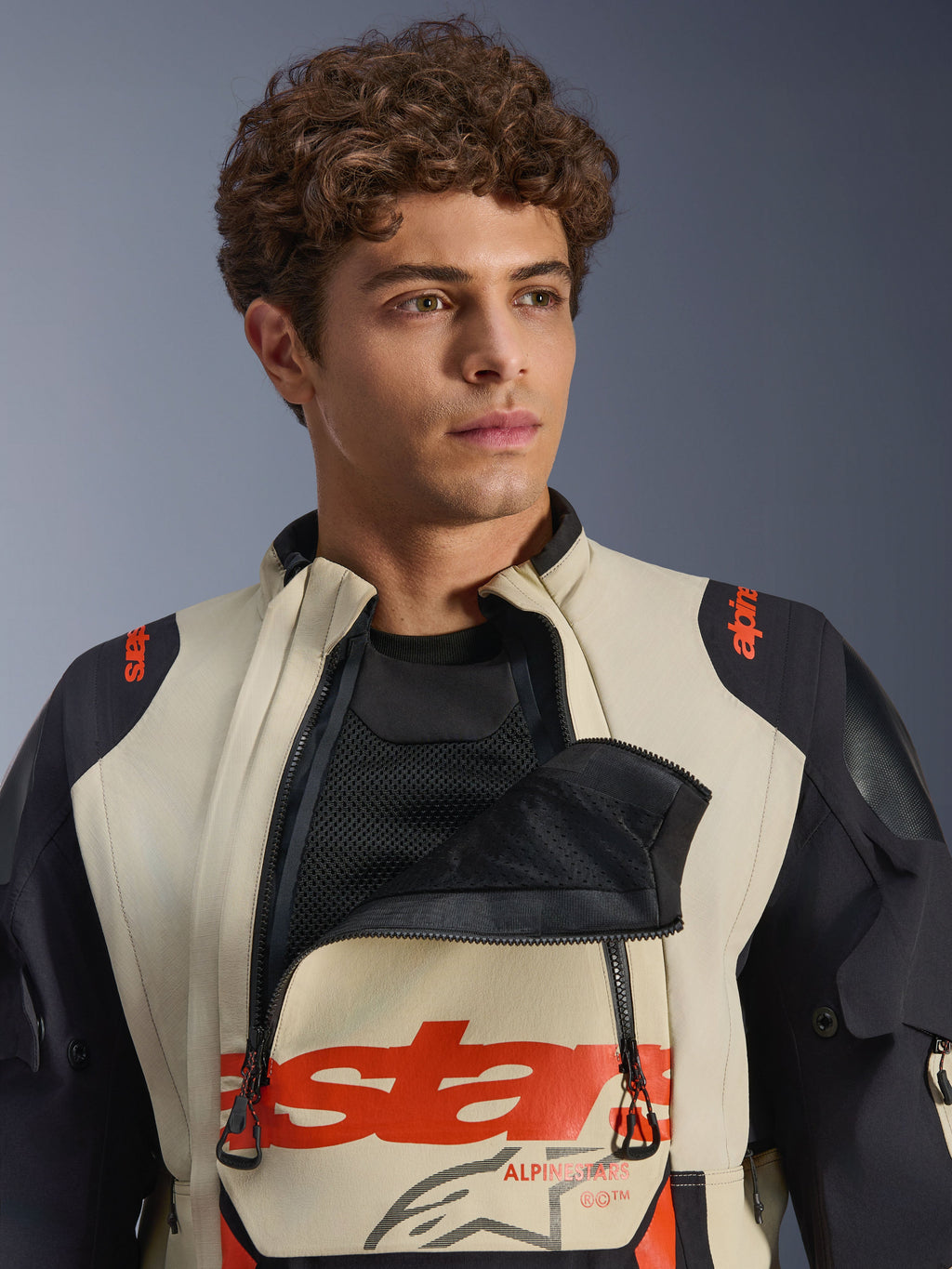 Alpinestars Halo Pro Drystar® XF laminerad jacka i Mastic Black, manlig modell som bär jackan med den främre ventilationspanelen på bröstet öppen för att visa mesh-underlager, röd logotyp och svarta axelpaneler, teknisk äventyrsutrustning för motorcykel