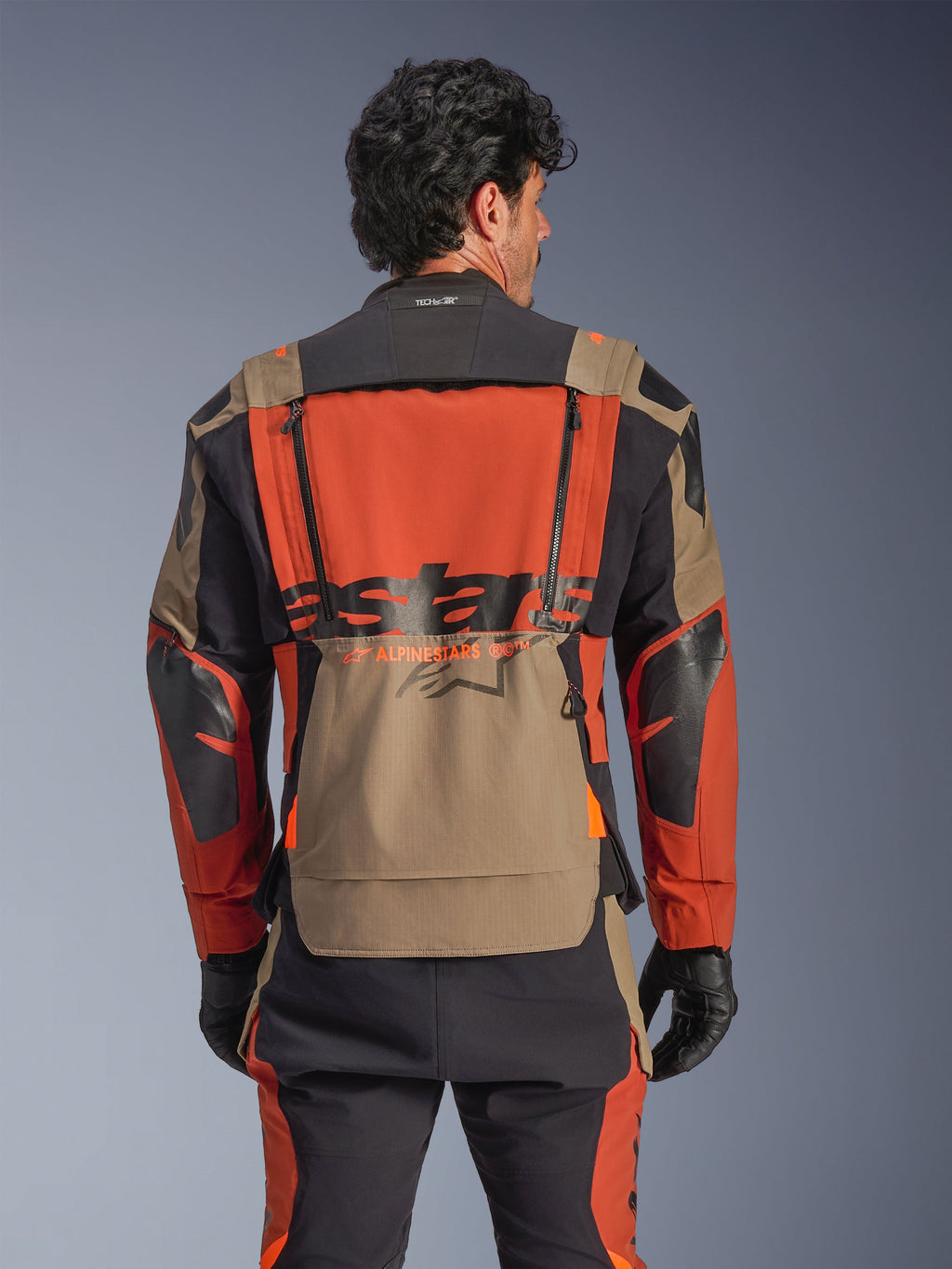 Alpinestars Halo Pro Drystar® XF laminerad jacka, färgställning Walnut Rust Black, sedd bakifrån, med stor orange ryggpanel med svart ASTARS-logotyp, valnötsfärgad nedre förvaringsficka och Tech-Air® Ready-krage, bärs med matchande äventyrsbyxor och svarta handskar
