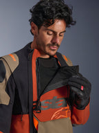 Alpinestars Halo Pro Drystar® XF laminerad jacka, färgställningen Walnut Rust Black, manlig modell som demonstrerar modulärt ventilationssystem genom att öppna bröstpanelen för att avslöja svart mesh, teknisk äventyrsmotorcykeljacka med rostfärgade och beige detaljer.