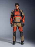 Manlig modell bär Alpinestars Halo Pro Drystar® XF-laminerad jacka och matchande byxor i Walnut Rust Black, modulär äventyrsmotorcykelutrustning med främre ventilationspaneler och dragkedjor, stylad med svarta motorcykelhandskar och stövlar.
