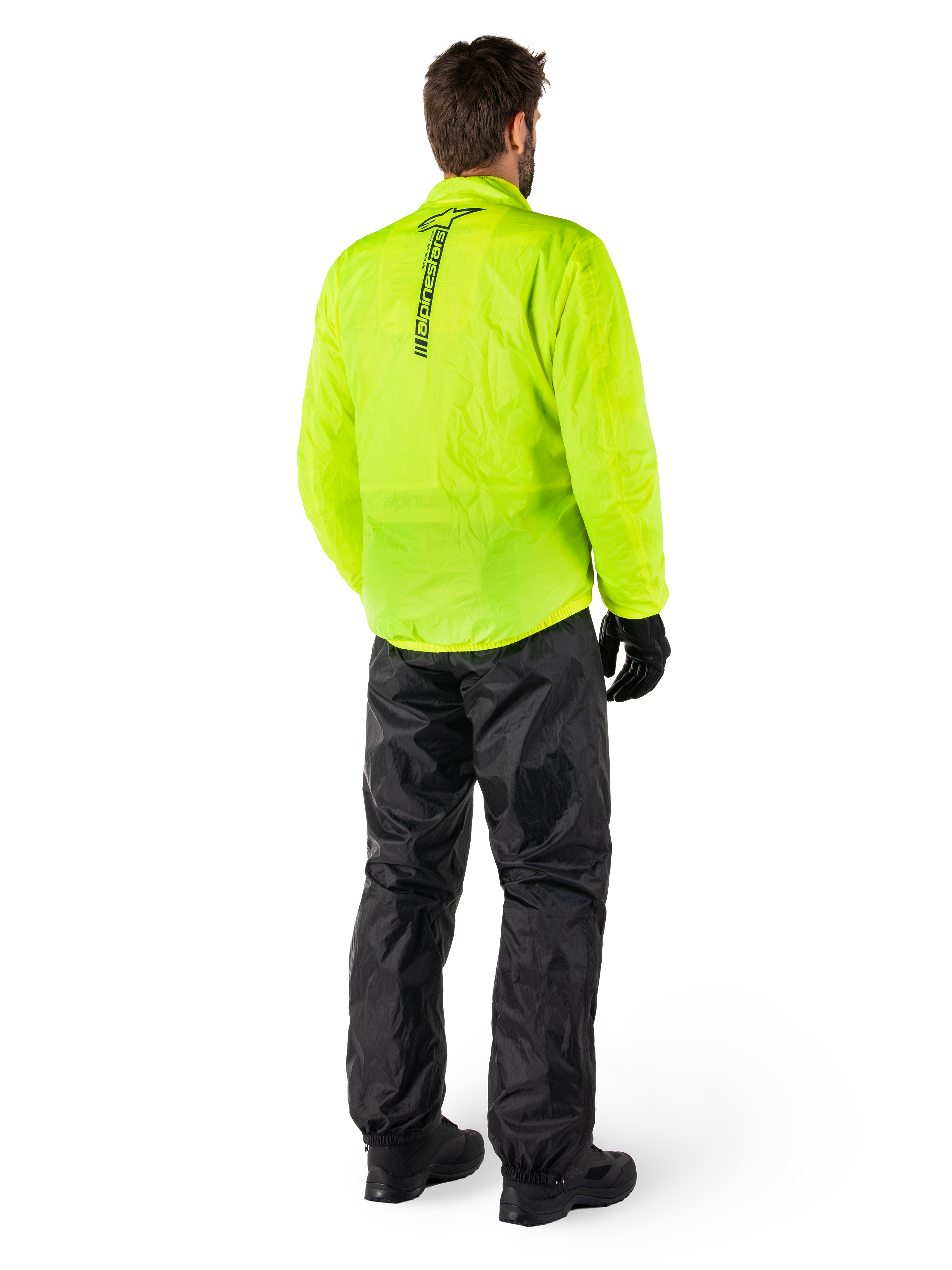 Person bakifrån som bär Alpinestars Hurricane Rain V2 Jacket i Yellow Fluo och Hurricane Rain V2 Pant i Black, vertikal logotyp på jackans rygg, vattentät motorcykelregnutrustning med svarta handskar och stövlar