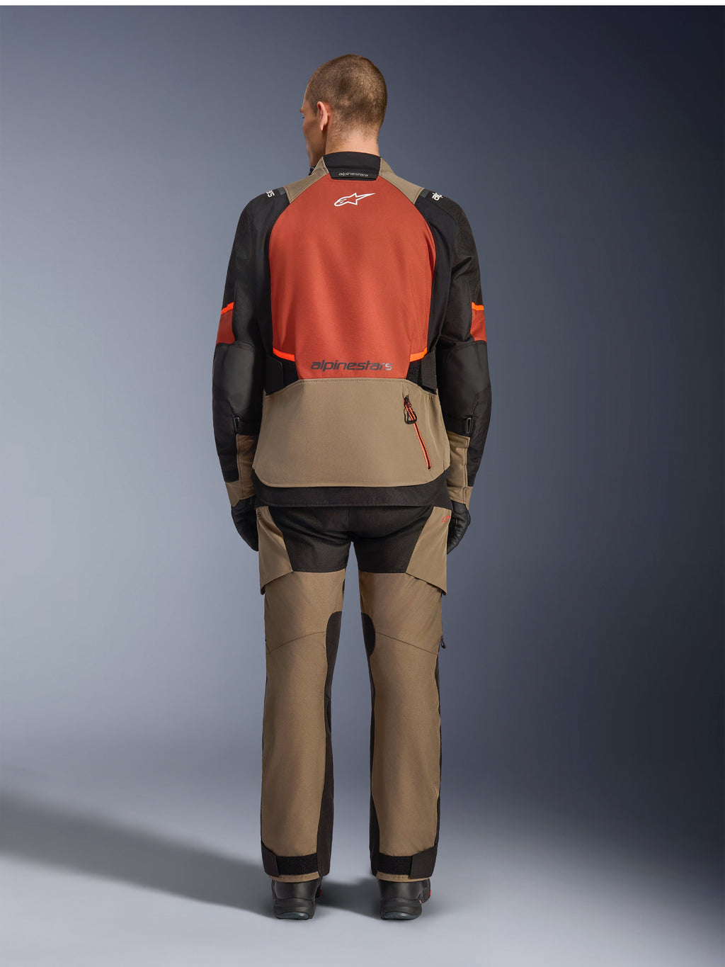 Alpinestars Andes V4 Drystar®-jacka, Walnut Rust Black, baksida av motorcykeljacka för touring med rostfärgad övre ryggpanel och valnötsfärgad nedre sektion, bärs med matchande äventyrsbyxor och svarta stövlar.
