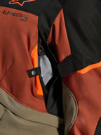 Alpinestars Andes V4 Drystar® Jacka, Walnut Rust Black, närbild på direkt ventilationsöppning med nätfoder, hållbart textilmaterial med orangea detaljer, tryckknapp och Alpinestars logotypdetalj