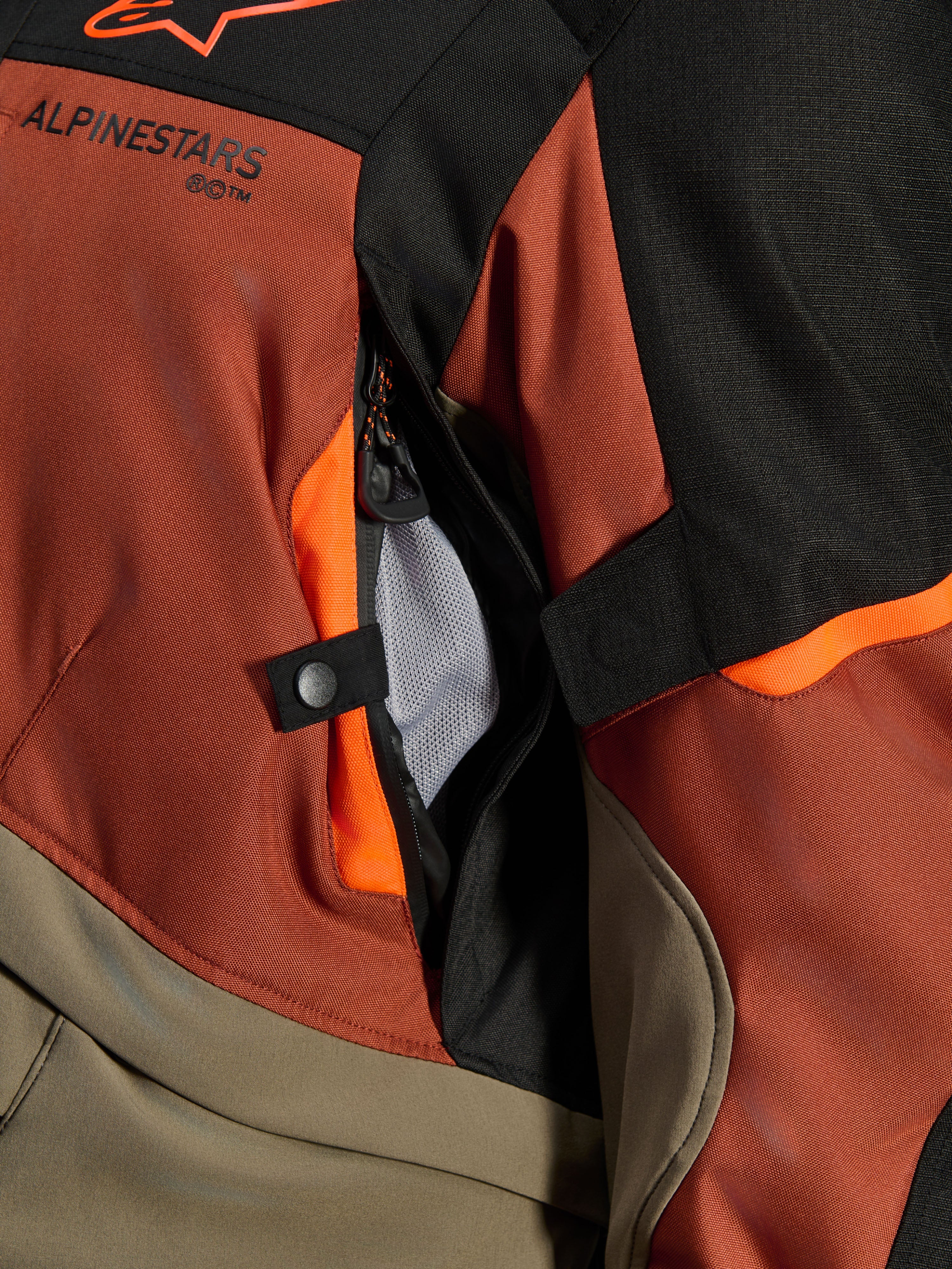 Alpinestars Andes V4 Drystar® Jacka, Walnut Rust Black, närbild på direkt ventilationsöppning med nätfoder, hållbart textilmaterial med orangea detaljer, tryckknapp och Alpinestars logotypdetalj
