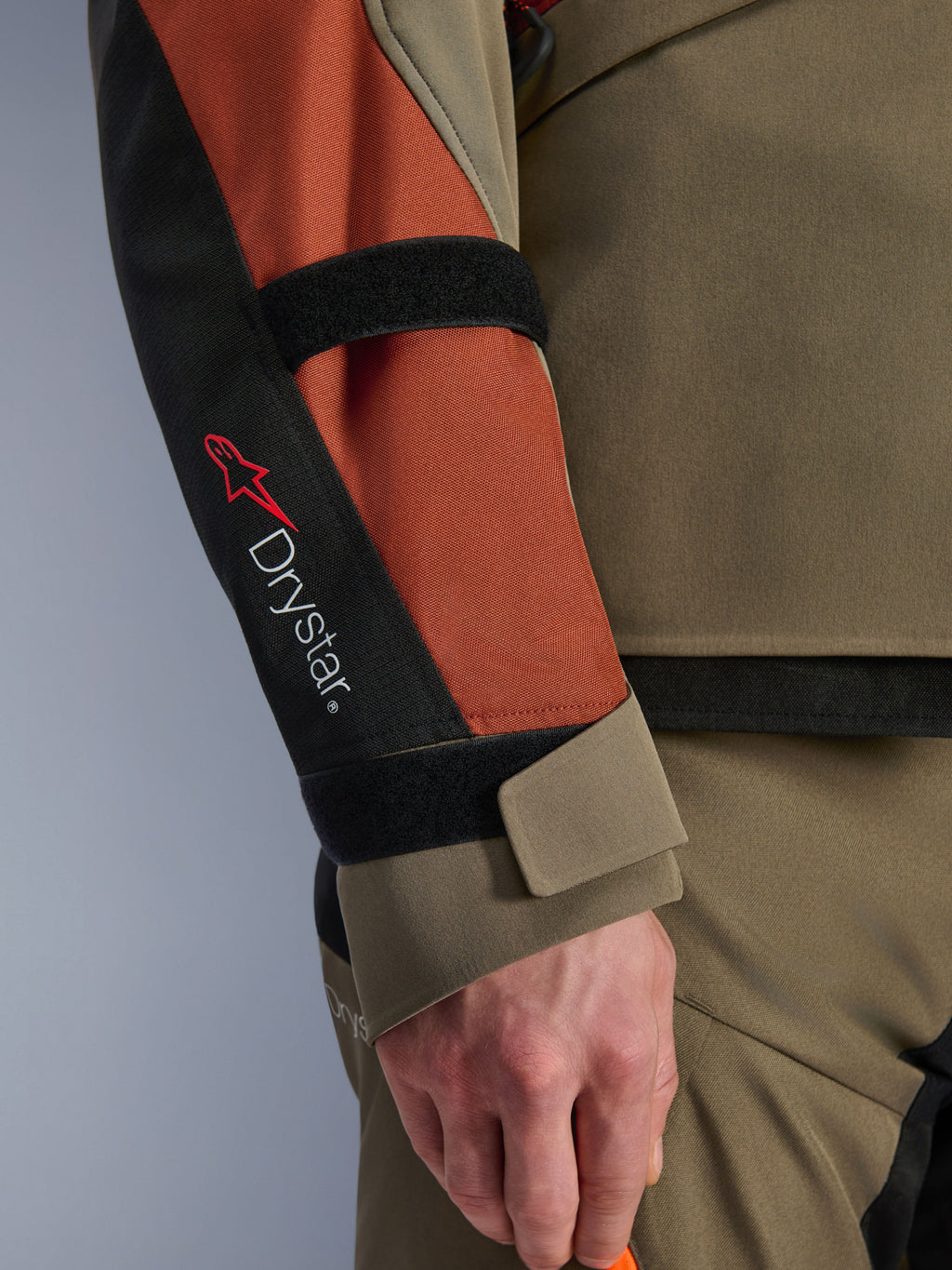 Alpinestars Andes V4 Drystar® jacka, motorcykeljacka, Walnut Rust Black, närbild av ärmen med Drystar®-märkning och röd stjärnlogotyp, med justerbara kardborreband vid underarm och handled, hållbar textildesign för äventyrstouring