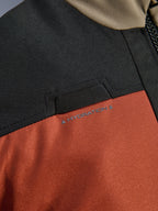 Närbild på Alpinestars Andes V4 Drystar®-jacka i Walnut Rust Black som framhäver den integrerade öglan för hydreringsslang på bröstet och den slitstarka konstruktionen i ripstop-textil.
