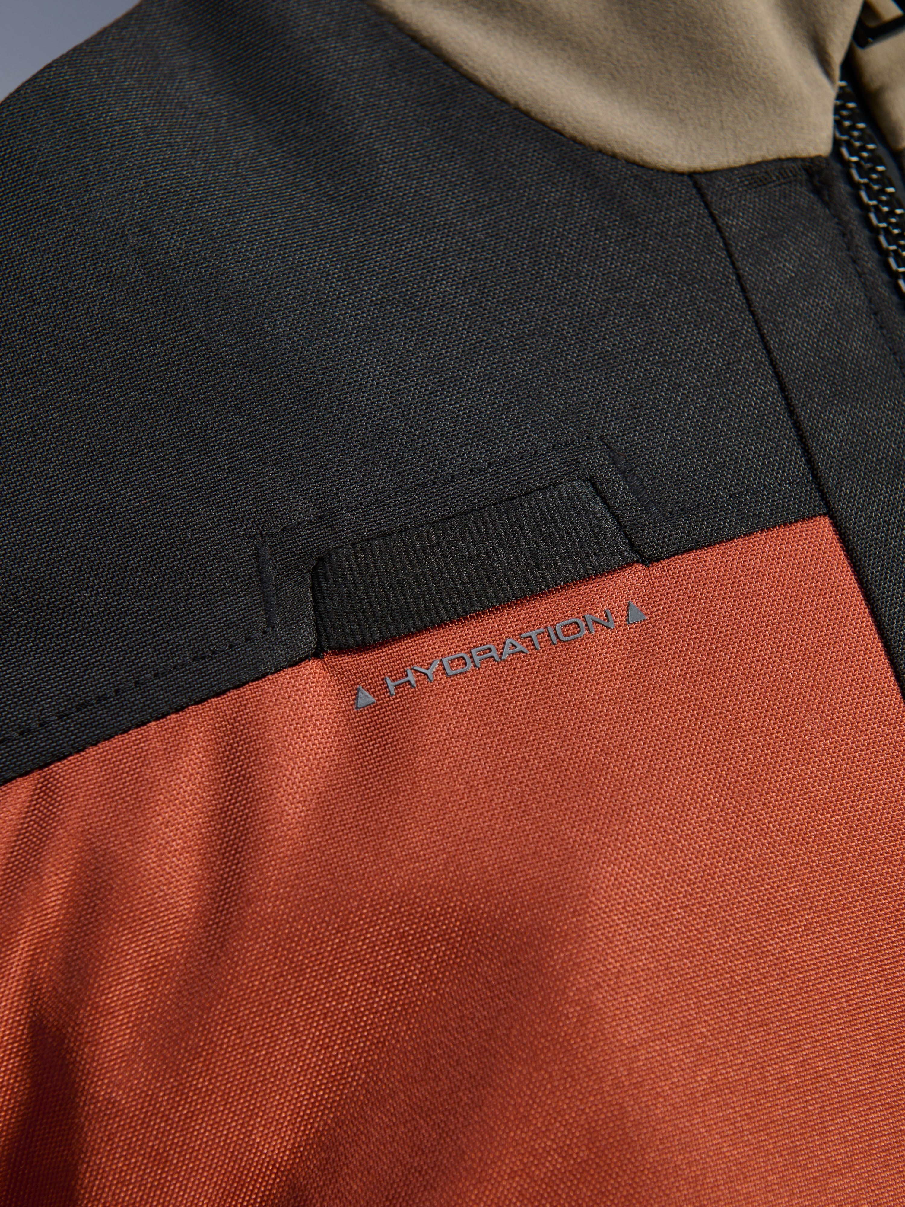 Närbild på Alpinestars Andes V4 Drystar®-jacka i Walnut Rust Black som framhäver den integrerade öglan för hydreringsslang på bröstet och den slitstarka konstruktionen i ripstop-textil.
