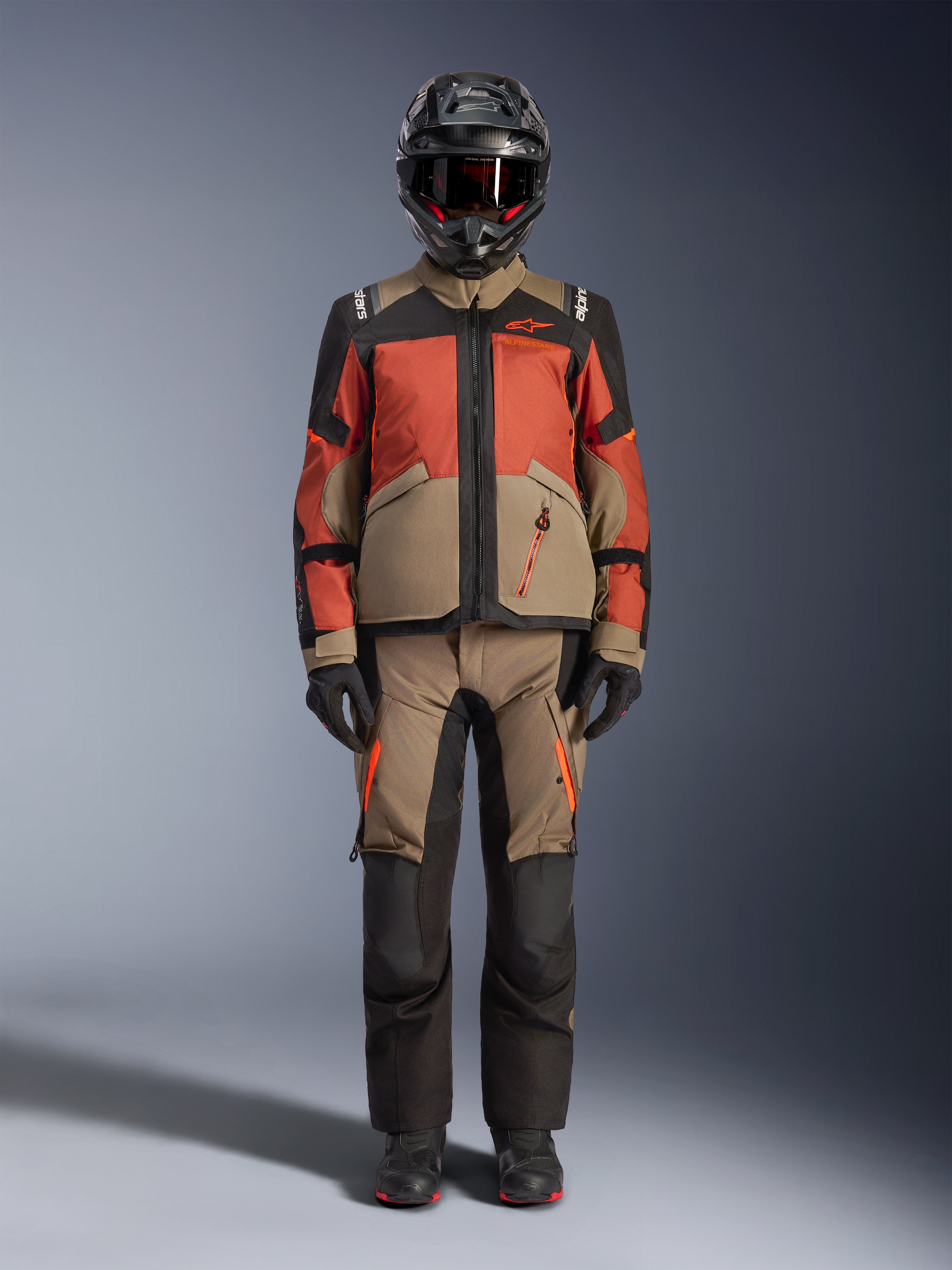 Äventyrsryttare klädd i Alpinestars Andes V4 Drystar® Jacket i Walnut Rust Black, matchad med tillhörande äventyrsbyxor, en svart hjälm med röda detaljer och goggles, samt svarta handskar, som visar en komplett touring-outfit för alla väder.