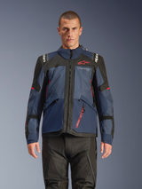 Alpinestars Andes V4 Drystar® Jacka, äventyrsmotorcykeljacka, Night Navy och Mood Indigo med svarta paneler, bärs av modell med svarta körbyxor, röd Alpinestars-logotyp på bröstet och röd dragkedjedetalj, hållbar textilkonstruktion för touring i alla väder.