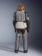 Alpinestars Andes V4 Drystar® jacka, äventyrsmotorcykeljacka, mörkgrå och isgrå med svarta och neongula accenter, vy bakifrån bärs med matchande byxor och svarta handskar, med en stor bakficka med gul dragkedja och förstärkta axel- och armbågspaneler