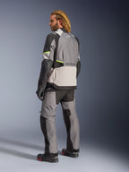 Alpinestars Andes V4 Drystar® Jacka, mörkgrå, isgrå, svart och neongul, vy bakifrån av förare som bär matchande adventure touring-byxor och stövlar, med förstärkta grå textilpaneler, neongula detaljer och Alpinestars-logotyper, motorcykelutrustning för alla väder.