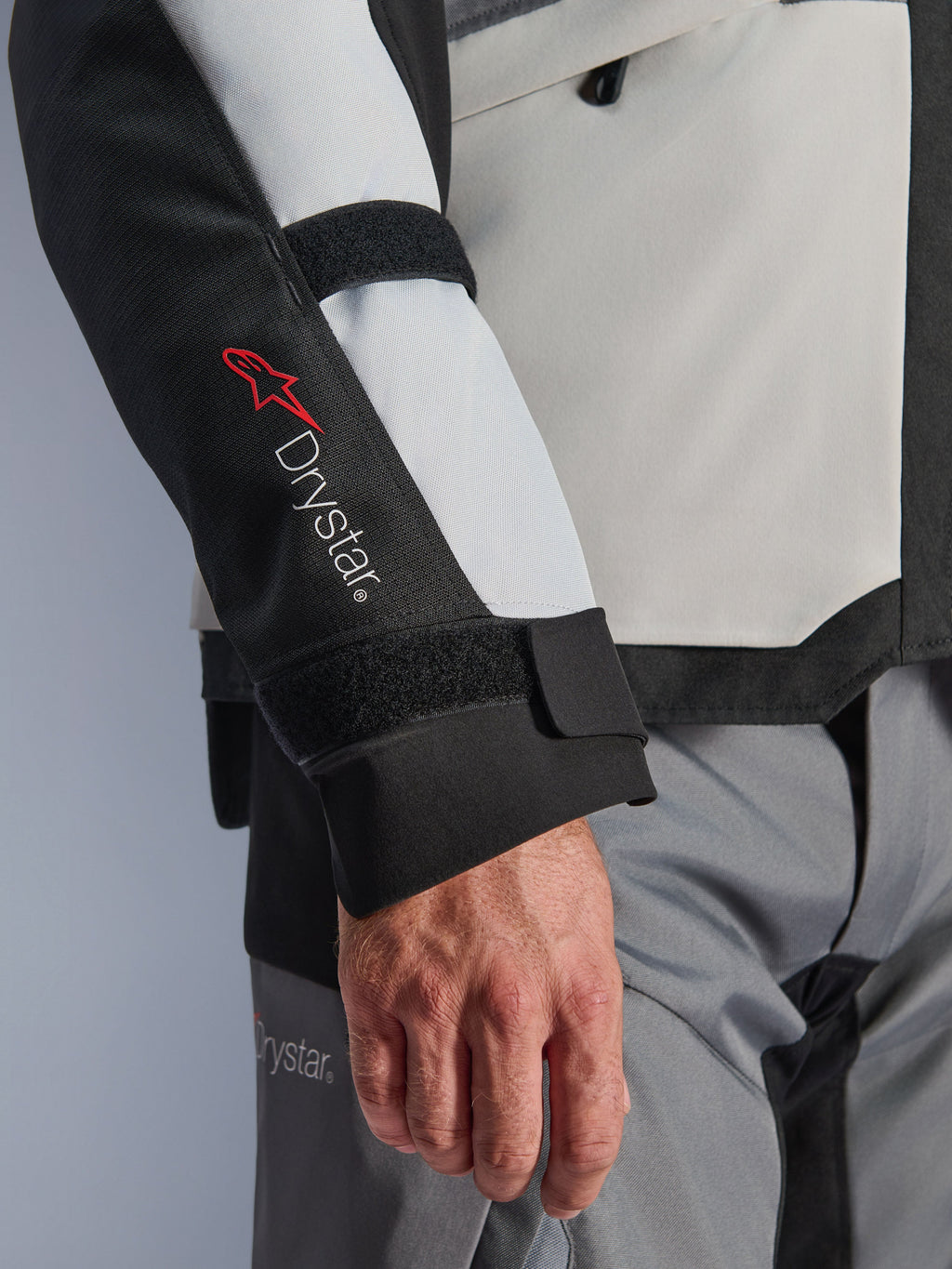 Alpinestars Andes V4 Drystar® jacka, äventyrsmotorcykeljacka, paneler i Ice Gray och svart, närbild på ärm med röd Drystar®-logotyp och justerbara remmar, funktionell textildesign för körning i alla väder