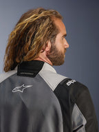 Närbild av ryggprofil på en man med långt vågigt hår som bär Alpinestars Andes V4 Drystar®-jacka i Dark Gray och Ice Gray, med textilpaneler och en vit Alpinestars-logotyp på ryggen, äventyrsmotorcykelkläder
