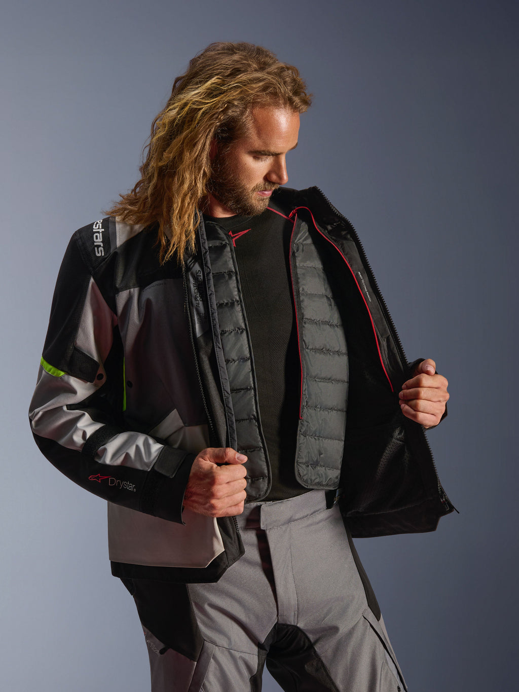 Alpinestars Andes V4 Drystar®-jacka, äventyrsmotorcykelutrustning i Dark Gray, Ice Gray och Yellow Fluo, manlig modell som visar det inre kviltade termofodret, bärs med matchande MC-byxor, prestandadesign för alla väder