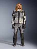 Manlig modell med långt blont hår i Andes V4 Drystar®-jacka i mörkgrått, isgrått, svart och gul fluo, kombinerat med matchande äventyrsmotorcykelbyxor och svarta stövlar, komplett teknisk körutrustning för touring i alla väder.
