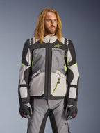 Alpinestars Andes V4 Drystar-jacka, äventyrs- och touringjacka för motorcykel, mörkgrå och isgrå med neongula detaljer, bärs av en modell med matchande byxor och handskar, textilkonstruktion med flera fickor för körning i alla väder