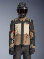 Alpinestars Andes V4 Drystar® Jacket, Walnut Mastic Black, adventure touring jacket featuring walnut brown and mastic cream panels, black sleeves, and bright orange accents, worn with a black motorcycle helmet, dark goggles, and black gloves