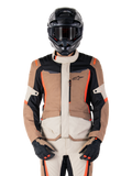 Alpinestars ST-1 Waterproof-jacka, Dark Khaki Sand Black Red Fluo, bärs av en förare med svart hjälm och handskar, adventure touring-utrustning med beige och bruna paneler och lysande röd-fluo detaljer, vy framifrån på vit bakgrund.