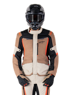 Alpinestars ST-1 Waterproof-jacka, Dark Khaki Sand Black Red Fluo, bärs av en förare med svart hjälm och handskar, adventure touring-utrustning med beige och bruna paneler och lysande röd-fluo detaljer, vy framifrån på vit bakgrund.