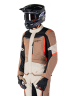 Alpinestars ST-1 Waterproof Jacket, adventure touring-jacka, mörk khaki, sand, svart och fluorescerande röd, bärs av en förare med svart motocrosshjälm och goggles, flerpanelsdesign med lastfickor och Alpinestars logotyp på bröstet