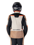 Alpinestars ST-1 Waterproof Jacket, Dark Khaki Sand Black Red Fluo, ryggvy, äventyrstouring-motorcykeljacka med en stor sandfärgad ryggpanel, svarta ärmar och rödfluorescerande detaljer, visas på en förare med en svart hjälm.
