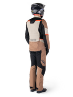 Alpinestars ST-1 Waterproof-jacka, äventyrstouringjacka, mörk khaki, sand, svart och röd fluo, vy bakifrån buren med matchande byxor och svart hjälm, med färgblockerade paneler och fluorescerande röda detaljer.