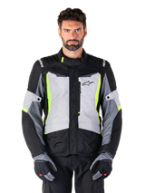 Alpinestars ST-1 Waterproof Jacket, adventure touring-motorcykeljacka, Ice Gray, svart och neongul, bärs av en man med matchande handskar och svarta byxor, neongula detaljer på bröstet och kragen, Alpinestars-logotyp på bröstet