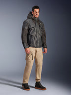 Manlig modell bär Alpinestars Mospher Waterproof Jacket i svart, en utility-inspirerad vattentät parka med huva och flera fickor, matchad med beige cargobyxor och svarta high-top sneakers, urban motorcykelutrustning för pendlare.
