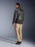 Man som bär Alpinestars Mospher Waterproof Jacket i svart, vy bakifrån och från sidan, kombinerad med beiga cargobyxor och svarta sneakers. Har en parkasdesign med huva i ripstop-tyg, Alpinestars-logotyp på ärmen och en modern urban motorcykelstil.