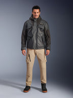 Manlig modell i Alpinestars Mospher Waterproof Jacket i svart, urban modern motorcykelutrustning, taktisk utility-design med flera funktionella fickor och huva, kombinerat med beige cargobyxor och svarta skor, helkroppsporträtt i studio.