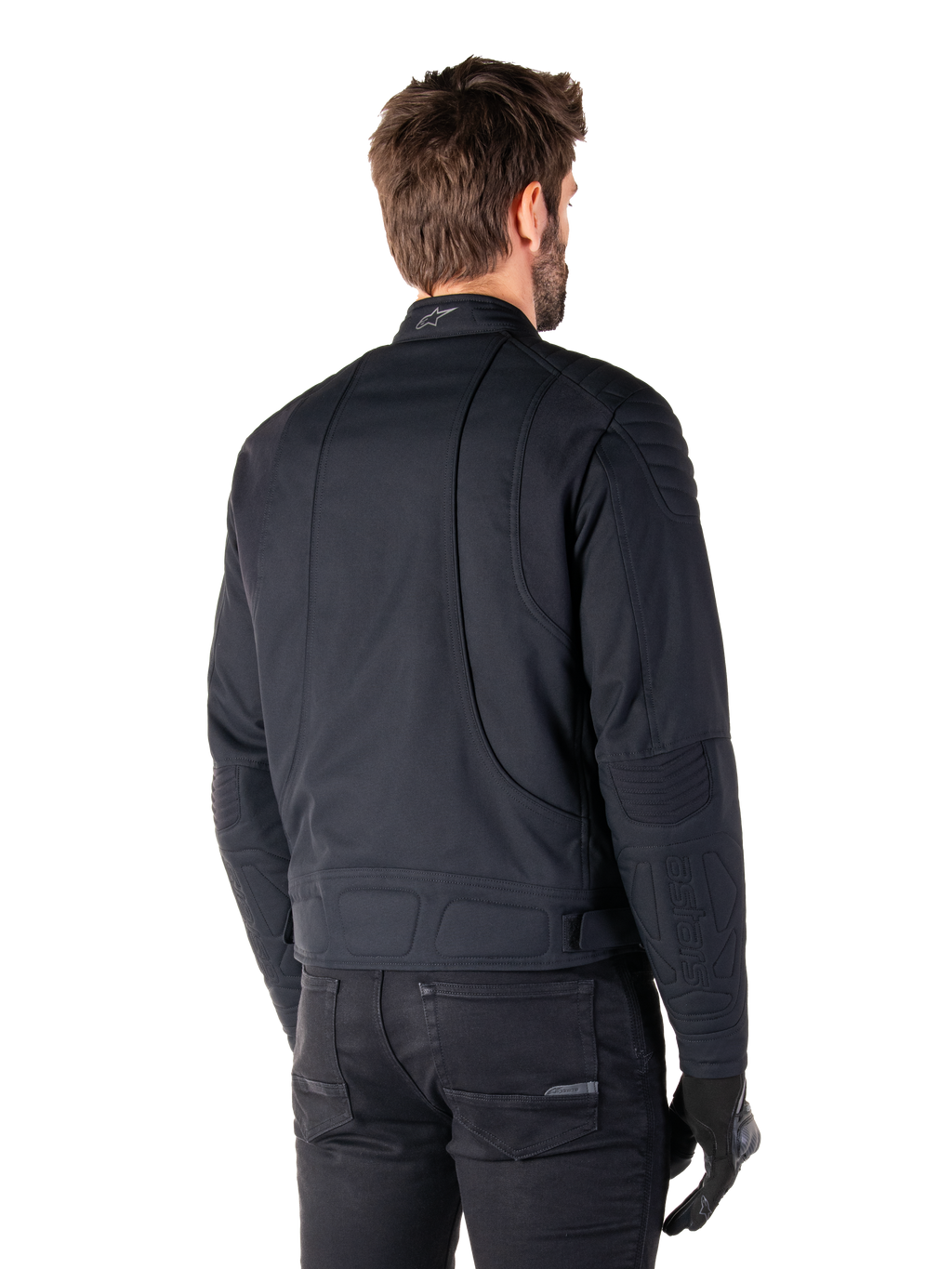 Alpinestars Clayton WR Jacket in Black, rear three-quarter view on a male model, urban motorcycle jacket with quilted padding on shoulders and elbows, technical stitch lines, and reflective logo on the collar, styled with black pants and gloves.