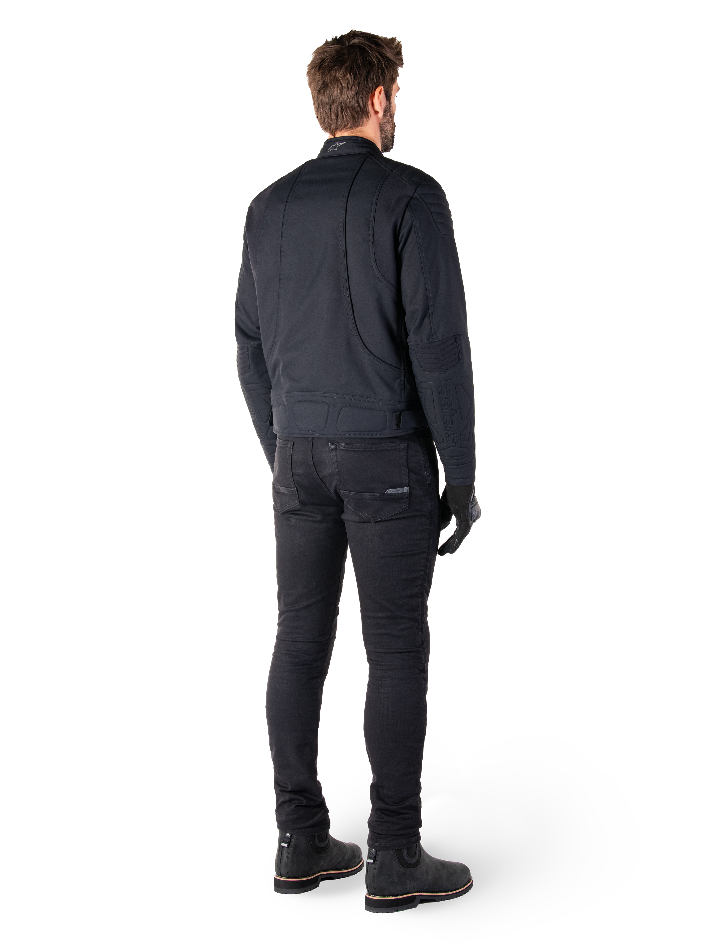 Rear view of a rider wearing the Alpinestars Clayton WR Jacket in Black, featuring quilted elbow and shoulder panels, ergonomic curved stitching, and reflective collar detailing, paired with black riding pants and boots for an urban motorcycle look.