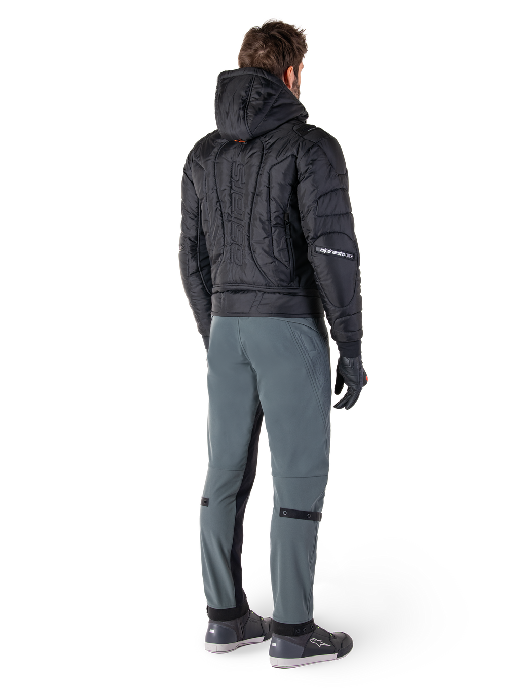 Alpinestars Mohobbs Waterproof Jacket, svart, baksida av quiltad vadderad bomberjacka med präglat vertikalt ordmärke på ryggen, stylad med grå körbyxor och svarta handskar, urban streetwear-inspirerad motorcykelutrustning