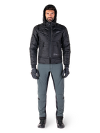Alpinestars Mohobbs Waterproof Jacket i svart, manlig modell som bär en quiltad vadderad bomberjacka med huva, matchad med grå MC-byxor, svarta handskar och svarta stövlar, urban modern motorcykelutrustning.