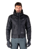 Alpinestars Mohobbs Waterproof Jacket, svart vadderad bomberjacka för motorcykel, quiltat polytyg med dragkedja fram och fickor med dragkedja, liten vit logotyp på bröstet, bärs av en modell med gråa byxor och handskar, urban streetwear-design för stadskörning.