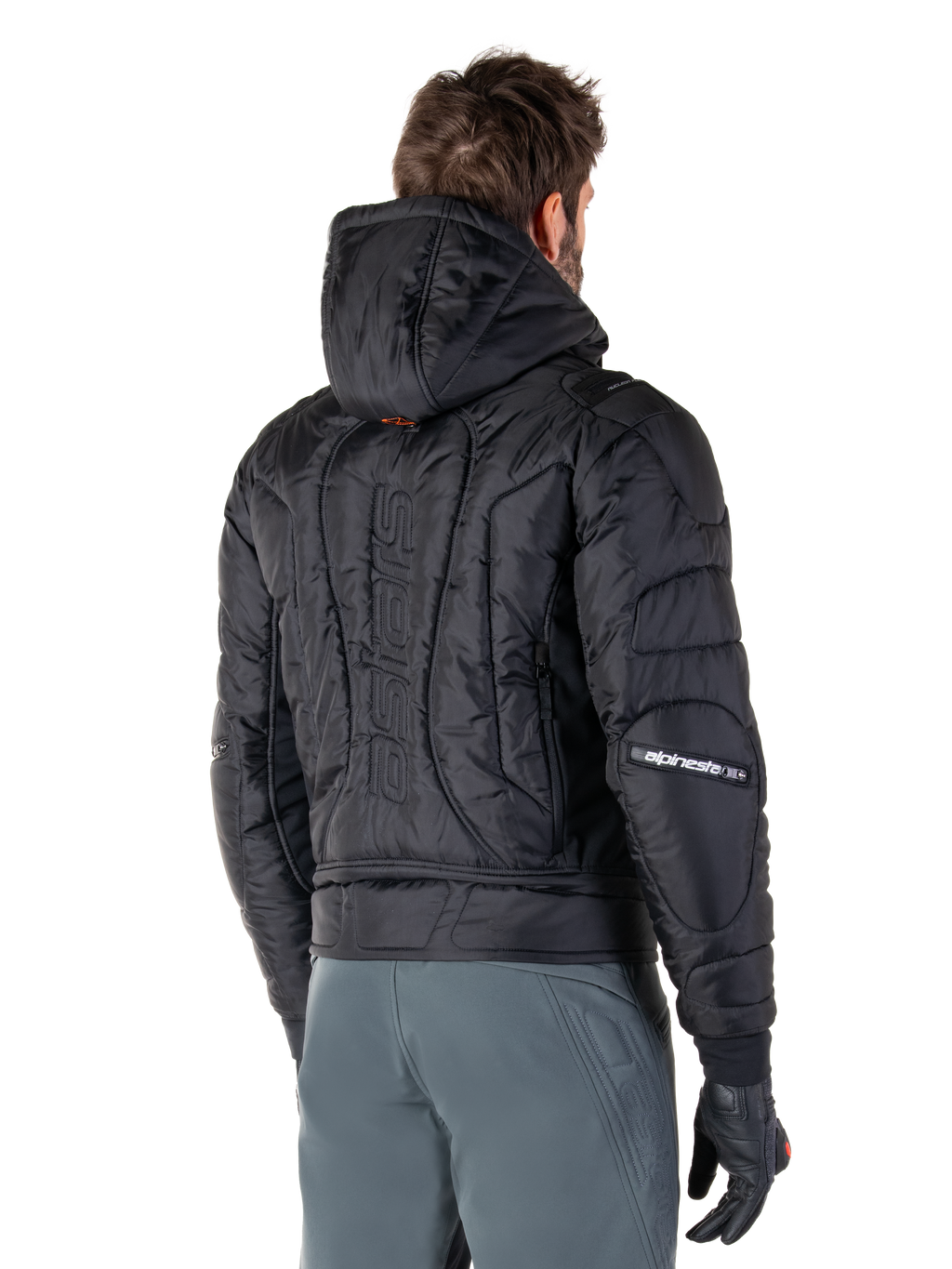 Alpinestars Mohobbs Waterproof Jacket, svart, vy bakifrån som visar quiltad vadderad konstruktion, huva, vertikalt astars-ordmärke på ryggen och Alpinestars-logotyper på ärmarna, bärs med gråa byxor och svarta handskar.